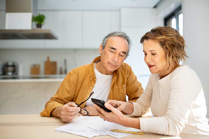 Senior couple sitting in kitchen with papers and bills