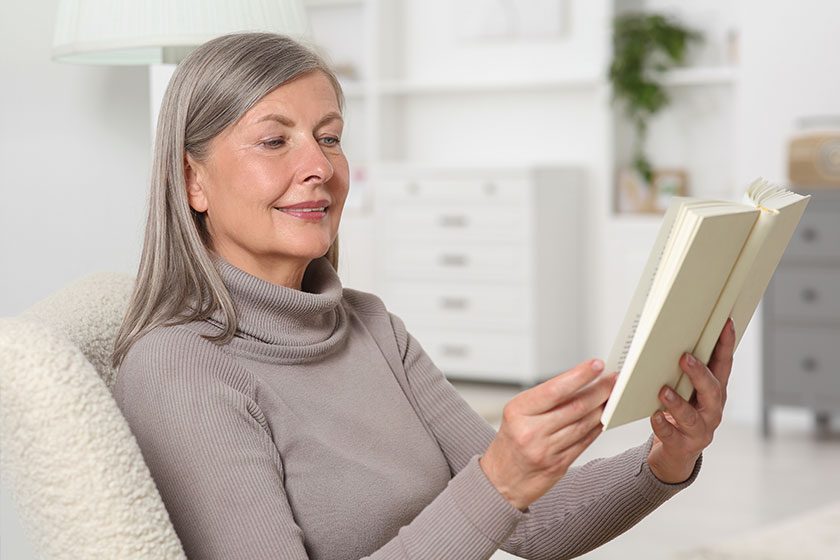 Beautiful senior woman reading book in armchair at home